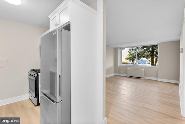 kitchen with white cabinets, appliances with stainless steel finishes, light wood-type flooring, and radiator