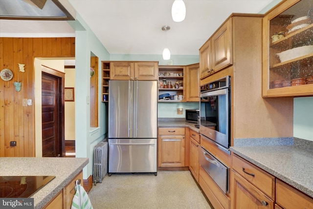 kitchen with light stone countertops, radiator heating unit, hanging light fixtures, wood walls, and appliances with stainless steel finishes