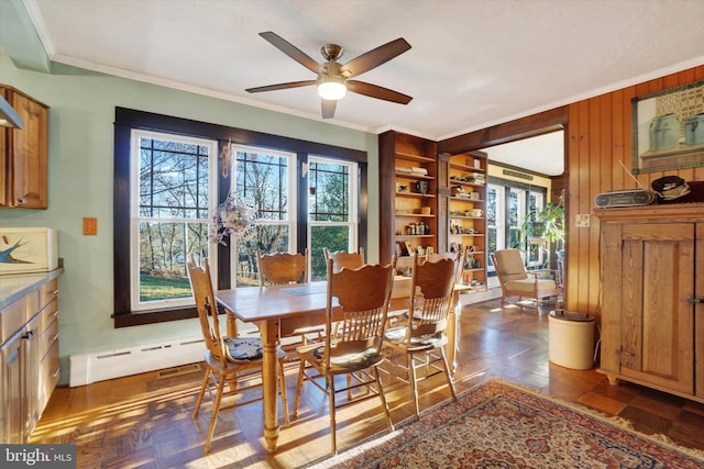 dining room featuring ornamental molding, ceiling fan, a baseboard heating unit, and wood walls