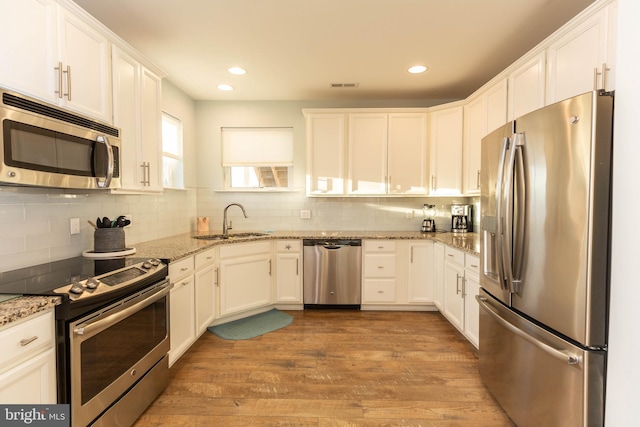 kitchen featuring white cabinets, sink, light stone countertops, wood-type flooring, and stainless steel appliances