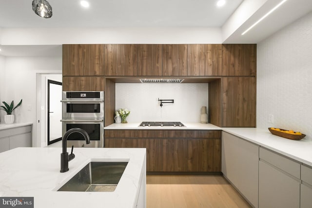 kitchen with double oven, light hardwood / wood-style flooring, sink, light stone counters, and gas stovetop