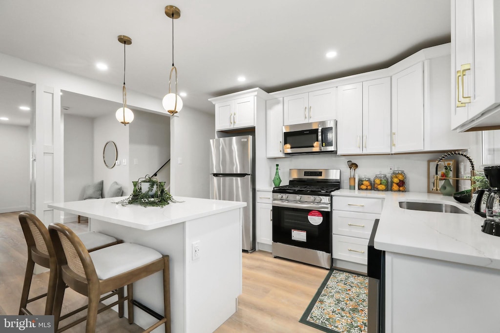 kitchen with stainless steel appliances, sink, light hardwood / wood-style flooring, white cabinetry, and hanging light fixtures