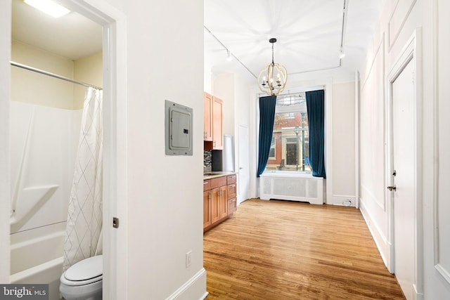 hall featuring light wood-type flooring, track lighting, a chandelier, radiator heating unit, and electric panel