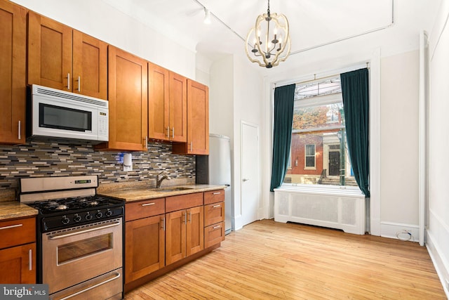 kitchen featuring gas stove, sink, radiator heating unit, a chandelier, and light wood-type flooring