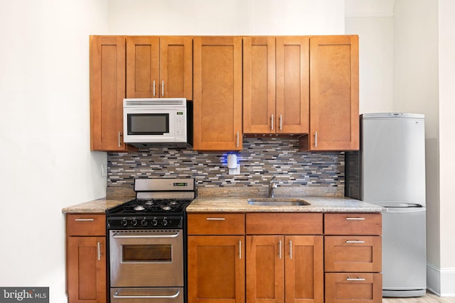 kitchen featuring light stone countertops, appliances with stainless steel finishes, backsplash, and sink