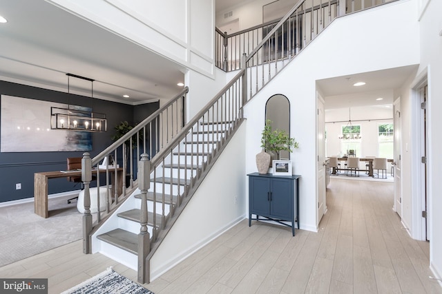 stairway with hardwood / wood-style floors, ornamental molding, and an inviting chandelier