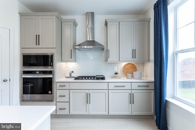 kitchen featuring appliances with stainless steel finishes, backsplash, gray cabinets, and wall chimney range hood