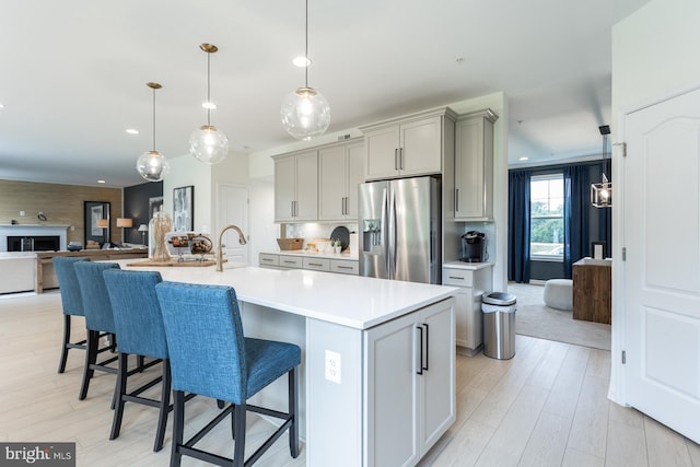 kitchen featuring a breakfast bar, a kitchen island with sink, pendant lighting, stainless steel fridge with ice dispenser, and gray cabinets