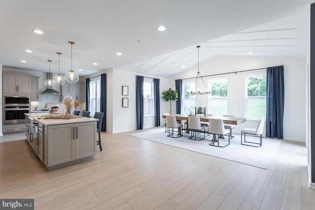 kitchen with gray cabinetry, an island with sink, hanging light fixtures, and lofted ceiling