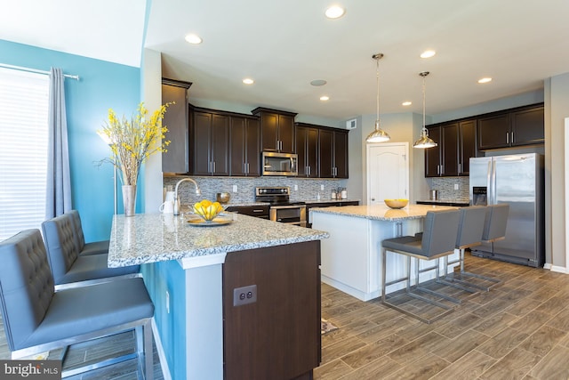 kitchen with a kitchen breakfast bar, light stone counters, pendant lighting, and stainless steel appliances