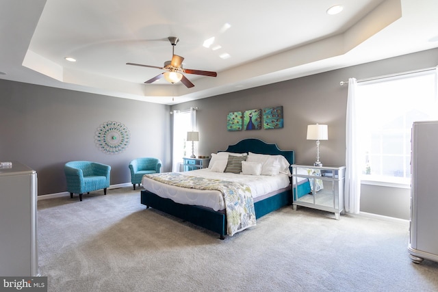 carpeted bedroom featuring a tray ceiling and ceiling fan