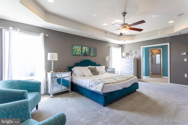 bedroom featuring ceiling fan, a raised ceiling, light colored carpet, and connected bathroom