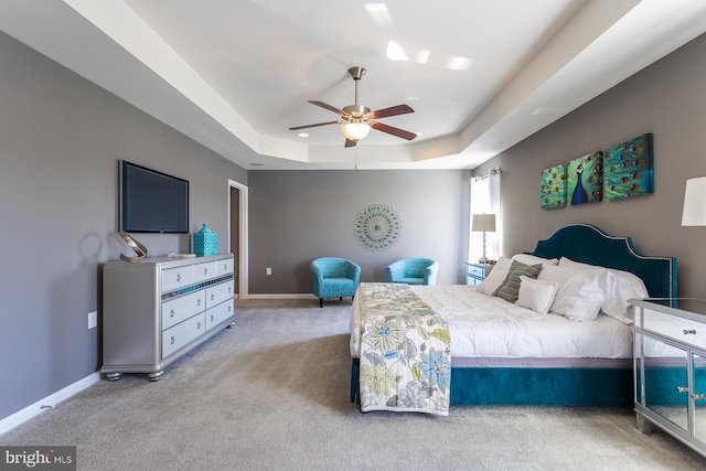 carpeted bedroom with a raised ceiling and ceiling fan