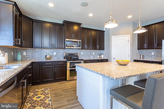 kitchen featuring light stone countertops, sink, pendant lighting, a breakfast bar, and appliances with stainless steel finishes