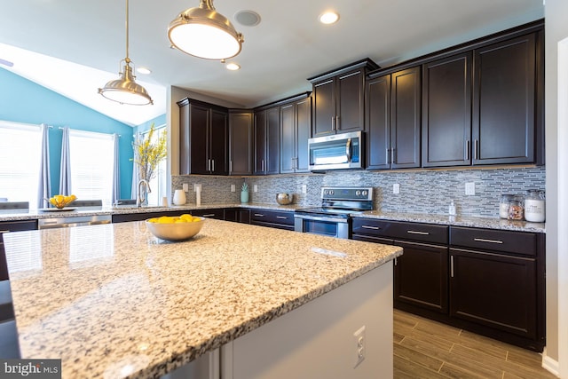 kitchen with light stone counters, decorative light fixtures, lofted ceiling, decorative backsplash, and appliances with stainless steel finishes