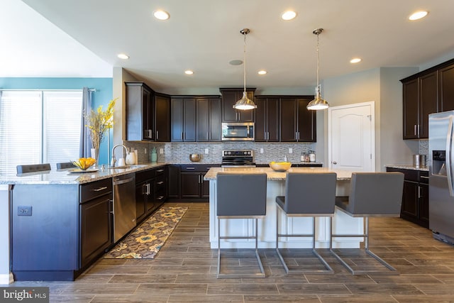 kitchen with light stone countertops, sink, a center island, pendant lighting, and appliances with stainless steel finishes