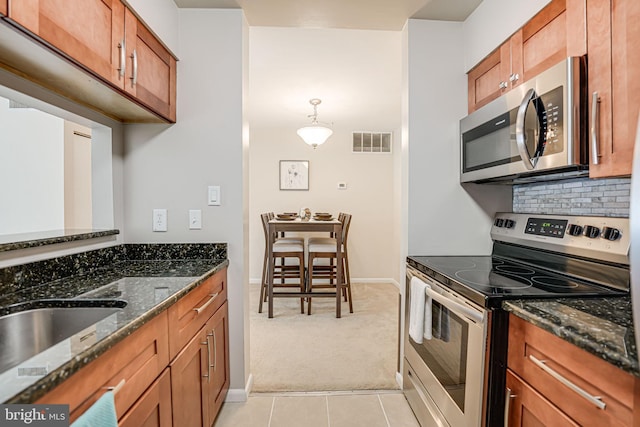 kitchen with sink, dark stone countertops, decorative light fixtures, light colored carpet, and stainless steel appliances