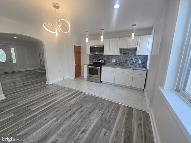 kitchen with decorative backsplash, appliances with stainless steel finishes, pendant lighting, light hardwood / wood-style flooring, and white cabinetry