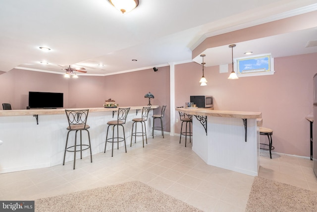 kitchen with a kitchen breakfast bar, ceiling fan, light tile patterned floors, hanging light fixtures, and crown molding