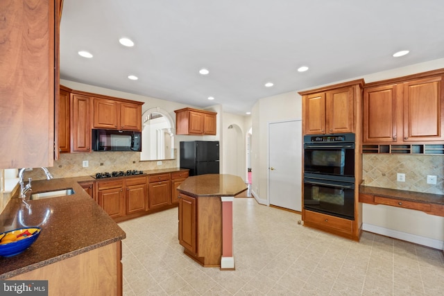 kitchen featuring tasteful backsplash, dark stone counters, sink, black appliances, and a center island