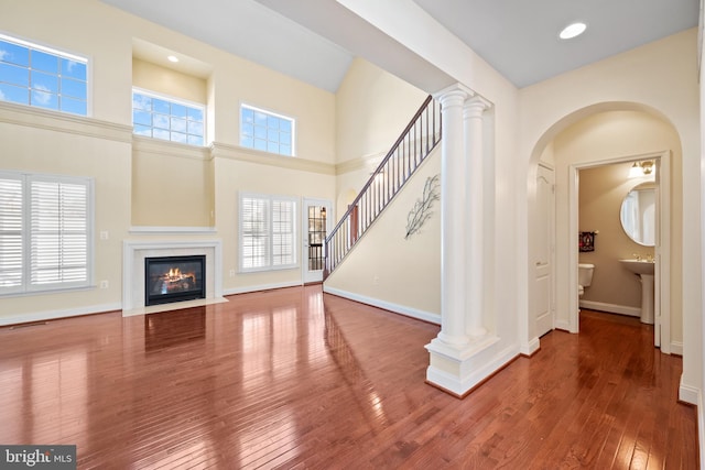 unfurnished living room with wood-type flooring, sink, a high ceiling, and decorative columns