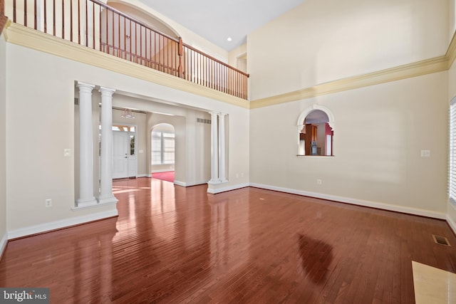 unfurnished living room featuring ornate columns, a high ceiling, and hardwood / wood-style flooring