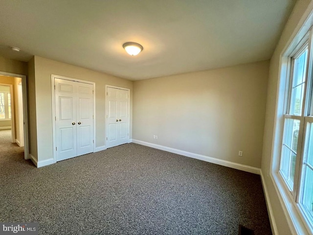 unfurnished bedroom with carpet flooring, multiple windows, and multiple closets