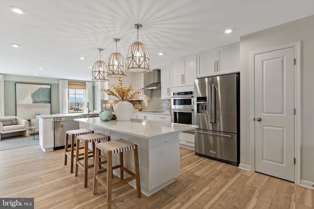 kitchen with appliances with stainless steel finishes, wall chimney exhaust hood, a center island, white cabinetry, and hanging light fixtures