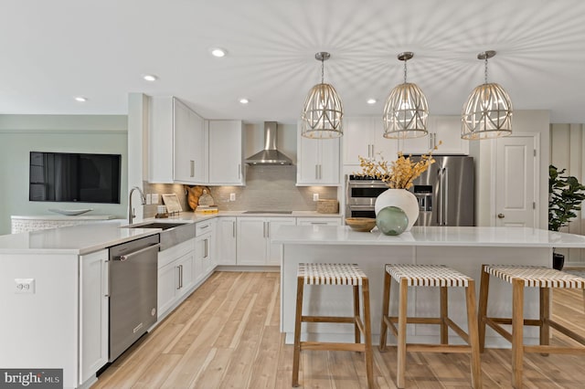 kitchen with white cabinetry, hanging light fixtures, stainless steel appliances, wall chimney range hood, and a kitchen island