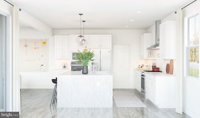 kitchen featuring gas stove, wall chimney range hood, pendant lighting, white cabinetry, and an island with sink