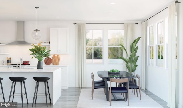 kitchen with a healthy amount of sunlight, white cabinetry, hanging light fixtures, and wall chimney range hood