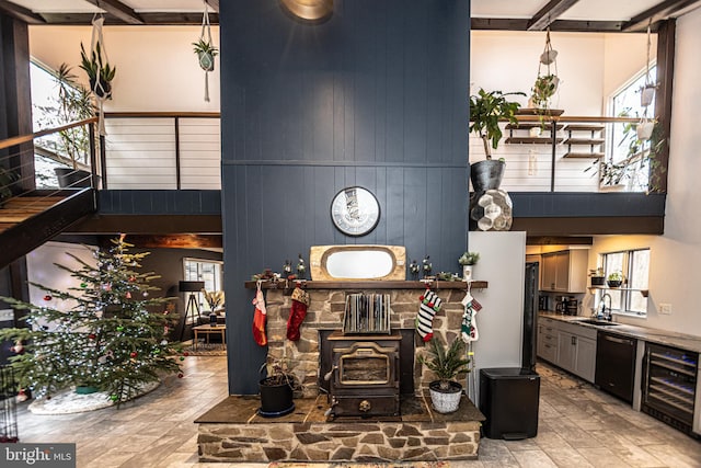 living room with beverage cooler, wooden walls, sink, beam ceiling, and a wood stove