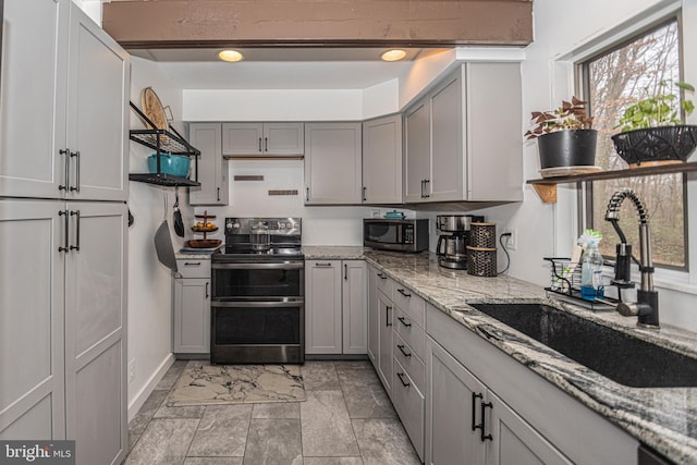 kitchen featuring appliances with stainless steel finishes, light stone counters, gray cabinetry, and sink