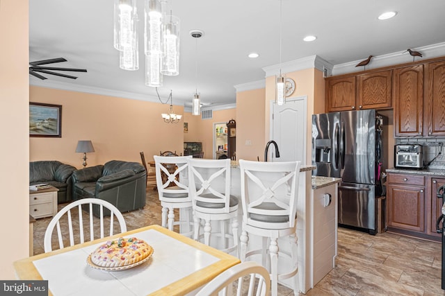 kitchen featuring stainless steel fridge, light stone counters, ceiling fan, crown molding, and hanging light fixtures