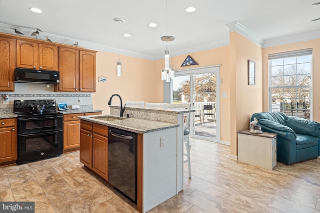 kitchen featuring sink, a kitchen breakfast bar, an island with sink, decorative light fixtures, and black appliances