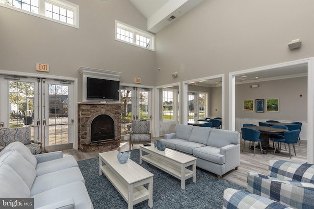 living room with french doors, light wood-type flooring, a stone fireplace, and a healthy amount of sunlight