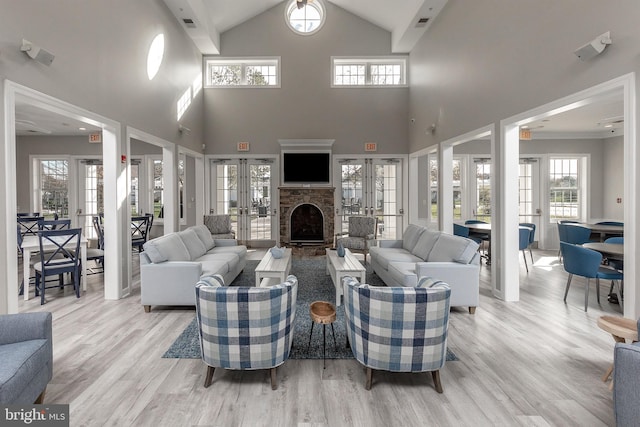 living room featuring light wood-type flooring, a fireplace, a towering ceiling, and french doors