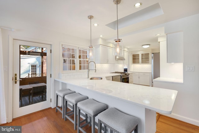 kitchen with kitchen peninsula, appliances with stainless steel finishes, a kitchen bar, white cabinets, and hanging light fixtures