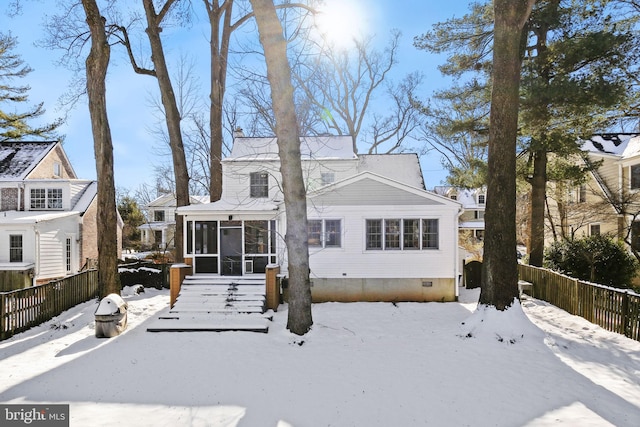 snow covered back of property featuring a sunroom