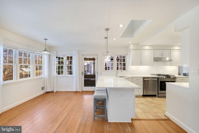 kitchen with decorative backsplash, appliances with stainless steel finishes, sink, white cabinets, and hanging light fixtures