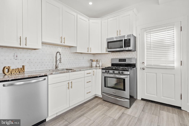 kitchen with light stone countertops, appliances with stainless steel finishes, tasteful backsplash, sink, and white cabinets