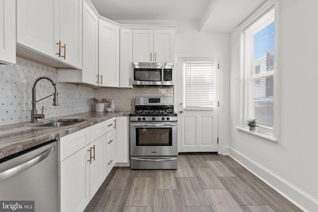 kitchen with white cabinets, sink, dark stone countertops, tasteful backsplash, and stainless steel appliances