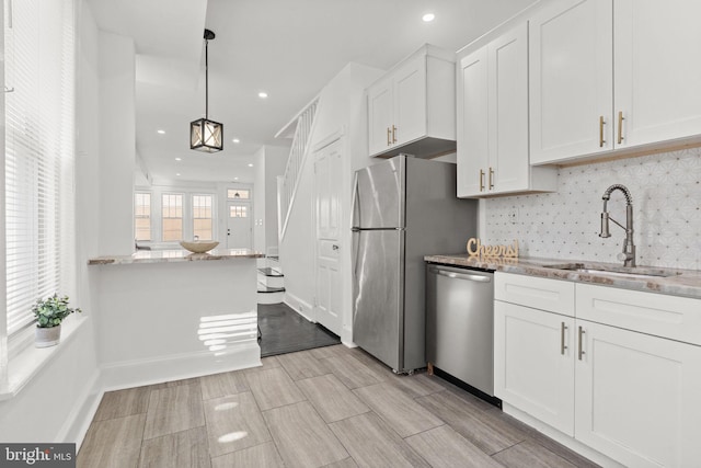 kitchen with light stone countertops, appliances with stainless steel finishes, sink, decorative light fixtures, and white cabinetry