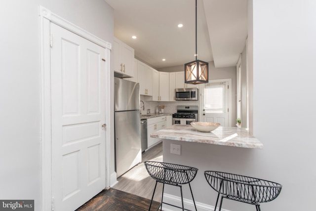 kitchen with white cabinetry, light stone countertops, kitchen peninsula, a breakfast bar area, and appliances with stainless steel finishes