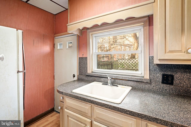 kitchen with sink, backsplash, white fridge, light brown cabinetry, and light wood-type flooring