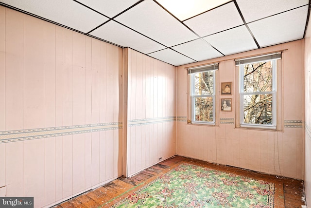 unfurnished room featuring a drop ceiling, wooden walls, and light hardwood / wood-style floors