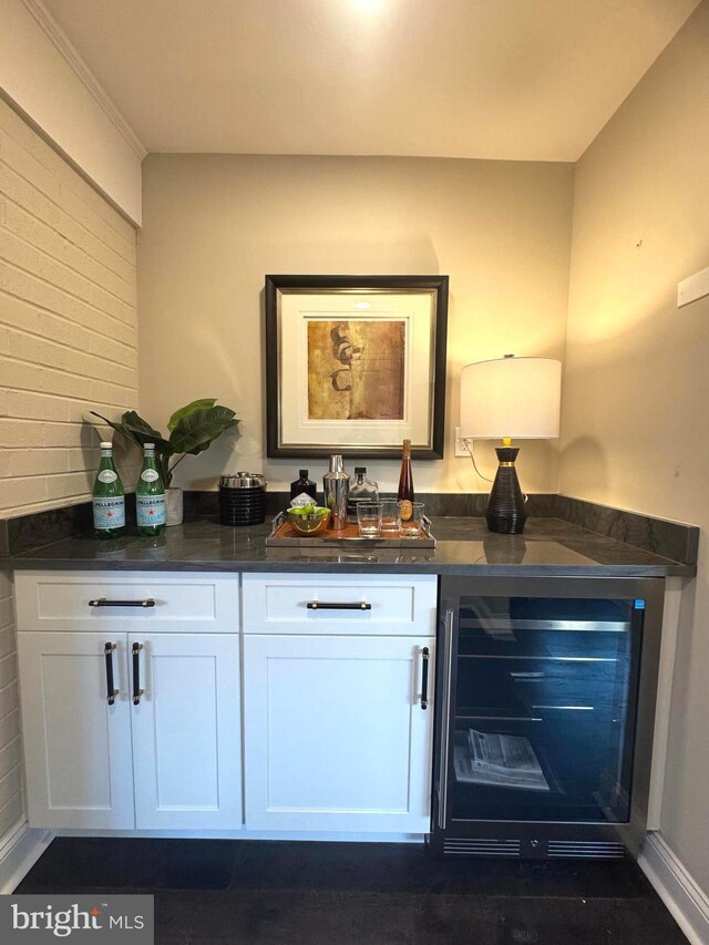 bar with wine cooler, dark stone countertops, and white cabinets