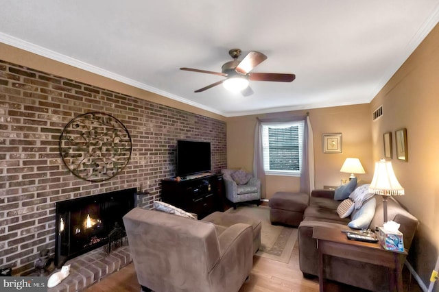 living room featuring ceiling fan, ornamental molding, a brick fireplace, and light wood-type flooring