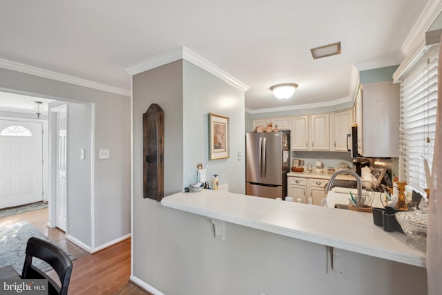 kitchen featuring a breakfast bar area, appliances with stainless steel finishes, kitchen peninsula, light hardwood / wood-style floors, and cream cabinetry