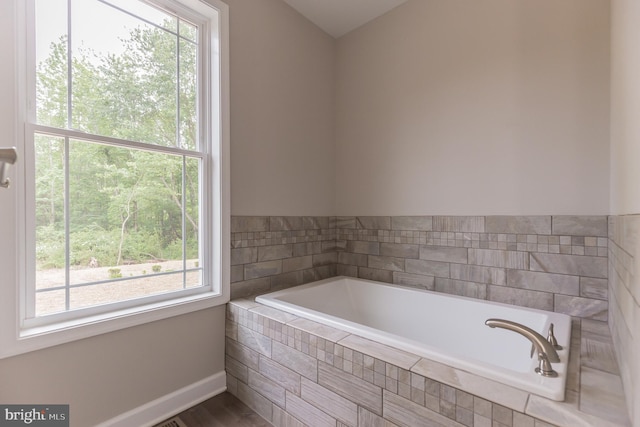 bathroom with hardwood / wood-style flooring, tiled tub, and a wealth of natural light